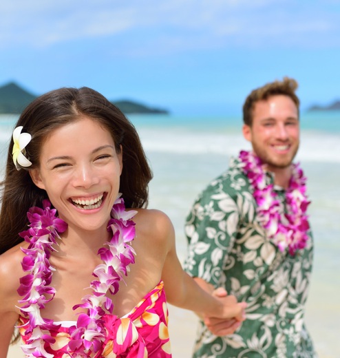 A happy couple each wearing a Hawaiian lei smile for the camera during their Maui proposal photoshoot.