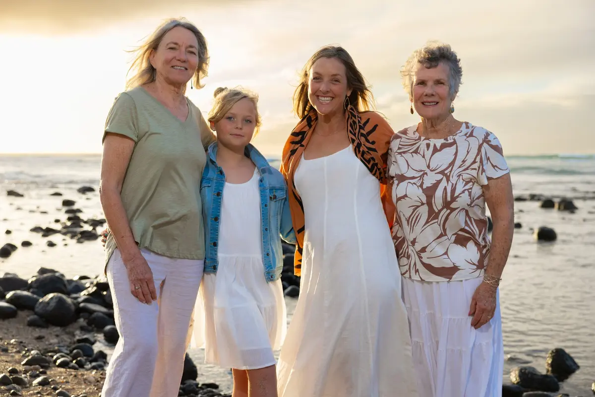 Photo from a family reunion in Maui. Three adults and one child pose together on the beach at sunset.