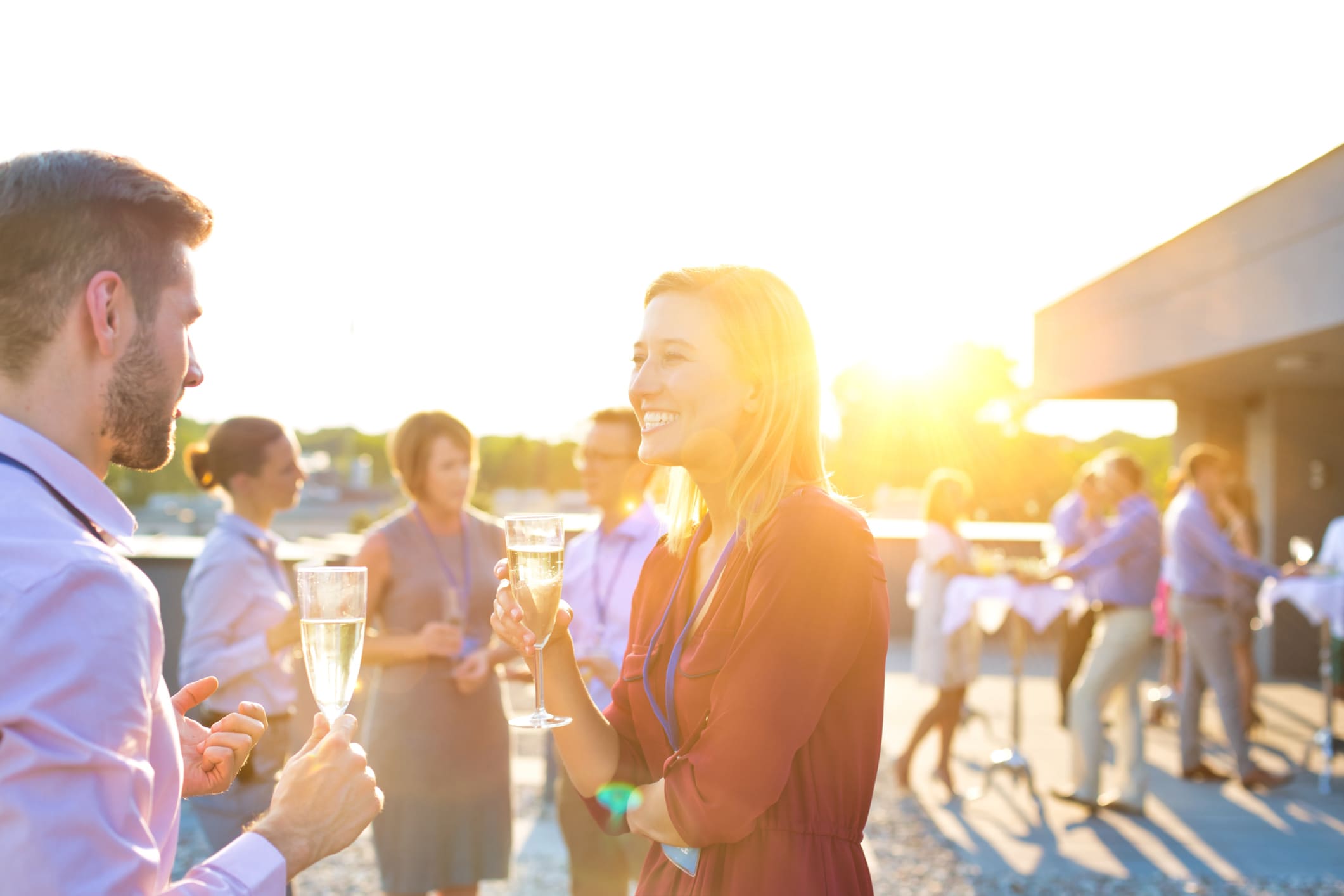 Smiling businesswoman drinking champagne while talking to colleague in rooftop team building event.
