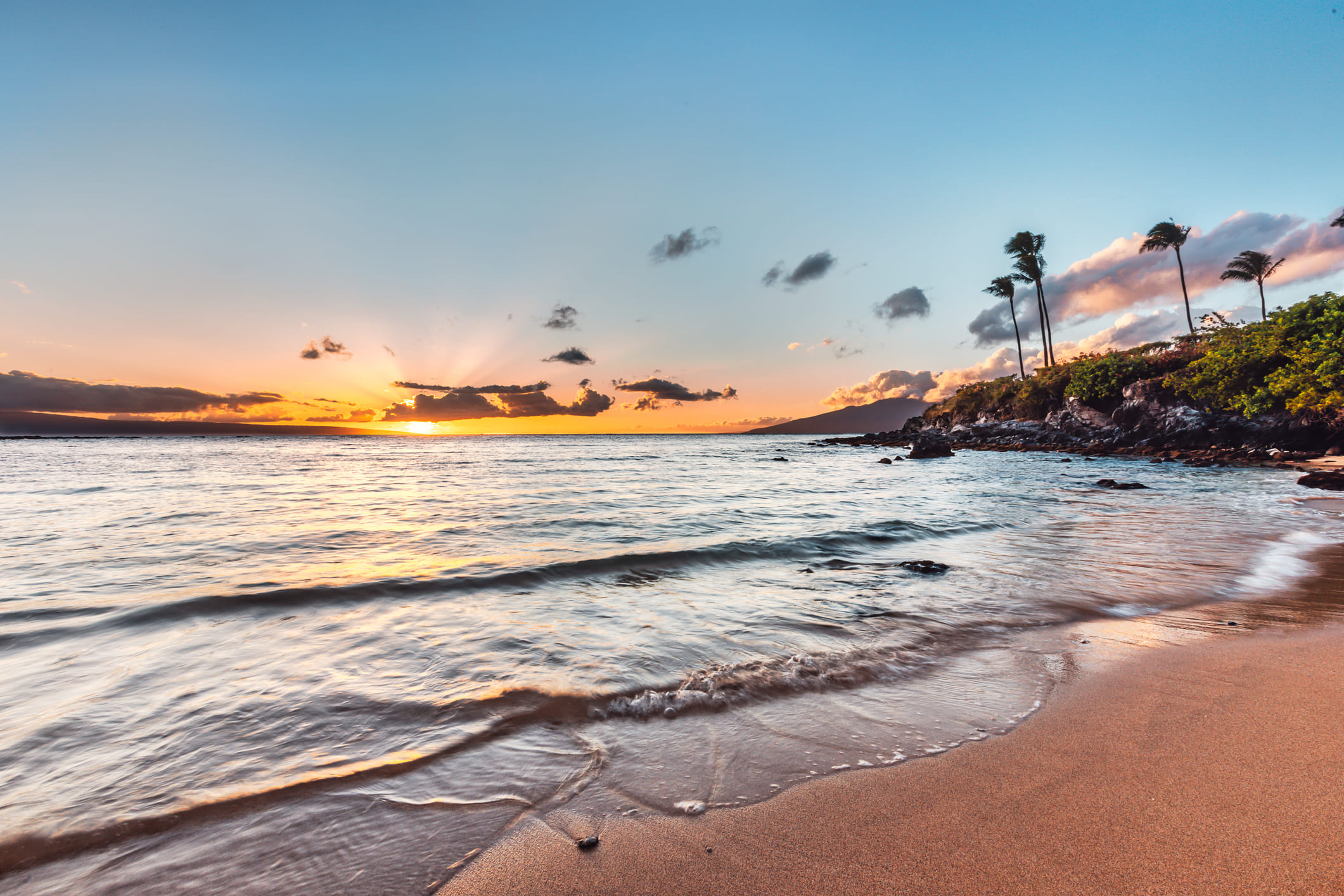 View from water's edge of Kapalua Bay at sunset with palm trees on the shore.